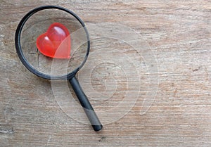 magnifying glass and decorative red hearts isolated on a brown wooden background minimalist trend.valentines day concept