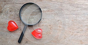 magnifying glass and decorative red hearts isolated on a brown wooden background minimalist trend.valentines day concept