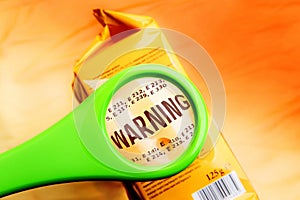 Magnifying glass on food additives label with word warning.