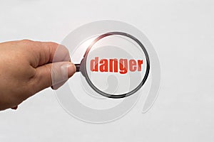 Magnifying glass in hand and a danger word on the white background