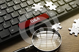 Magnifying glass, jigsaw puzzle and computer keyboard with red button written with QNA or Questions and Answers