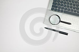 Magnifying glass on laptop keyboard and pen with copy space. Information search concept