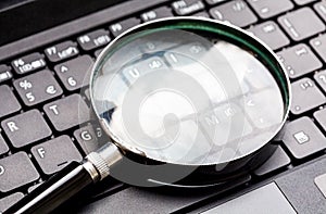 Magnifying glass laying on a laptop keyboard. Loupe on a netbook keys.Technology file search tool concept, data forensics photo