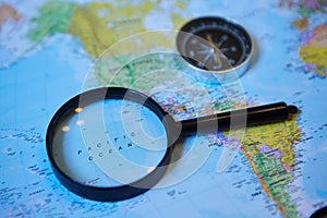 The magnifying glass is located on the world map and magnifies the Pacific ocean. There`s a compass next to it. Concept of travel