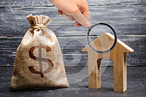 Magnifying glass is looking at a bag with money and a house with a large doorway. Concept of real estate acquisition