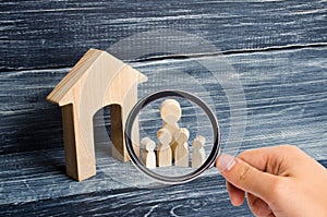 Magnifying glass is looking at the Big family is standing near the house. Wooden figures of persons stand near a wooden house.