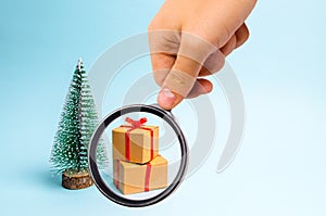 Magnifying glass is looking at the Christmas tree and gift on a blue background. Minimalism. Family holiday, Christmas