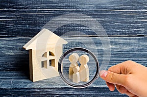 Magnifying glass is looking at the Family is standing near the house. Wooden figures of persons stand near a wooden house.