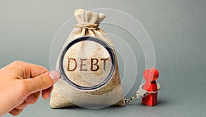 A magnifying glass is looking at a money bag with the word Debt and a borrower is bound by handcuffs. Mandatory payment of debt.