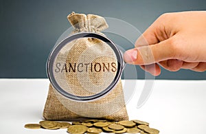 A magnifying glass is looking at a money bag with the word Sanctions. The imposition of economic and political sanctions on the