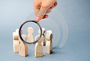 Magnifying glass is looking at people stand in a circle on a gray background. Wooden figures of people. A circle of people