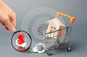 Magnifying glass is looking at a person is handcuffed to a house on a supermarket cart. Financial dependence, unavailable housing