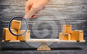 Magnifying glass is looking at the piles of boxes on the scales. Trade balance and calculation by barter. import and export of