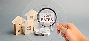 A magnifying glass is looking at a poster with the word Low rates and wooden house. The concept of reducing interest rates on photo