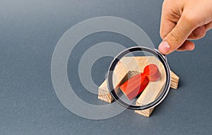 Magnifying glass is looking at a red figurine of a man and a fallen house on a gray background. accident or disaster.