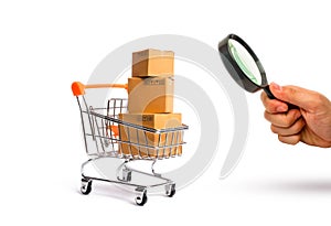 Magnifying glass is looking at the Supermarket cart with boxes, merchandise: the concept of buying and selling goods and services