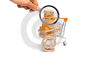 Magnifying glass is looking at the Supermarket cart with boxes, merchandise: the concept of buying and selling goods and services