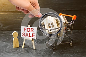 Magnifying glass is looking at the supermarket cart with houses and man with a poster for sale. concept of selling a home