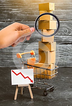 Magnifying glass is looking at the supermarket cart loaded with lots of boxes and a red down arrow. concept of sales drop
