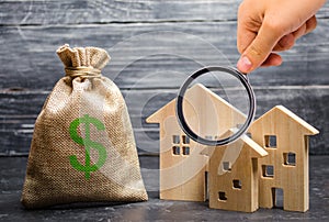 Magnifying glass is looking at the three houses near a bag with money. real estate acquisition and investment.