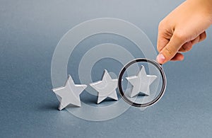 Magnifying glass is looking at three stars on a gray background. The concept of rating and evaluation. The rating of the hotel