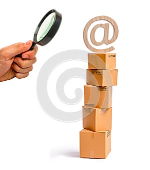 Magnifying glass is looking at the tower of cardboard boxes and an email symbol on top. concept of online sales, shopping