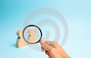 Magnifying glass is looking at the Two people stand together and talk. Two wooden figures of people conduct a conversation