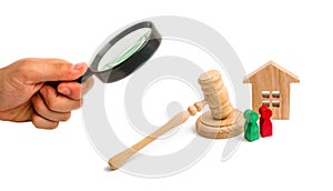 Magnifying glass is looking at the Wooden apartment house with keys and a judge hammer on a white background. The concept of the t