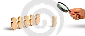 Magnifying glass is looking at the Wooden figures of people stand in the formation and listen to their leader. Business training,