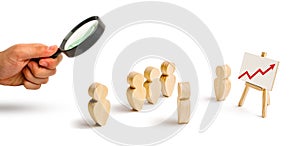 Magnifying glass is looking at the Wooden figures of people stand in the formation and listen to their leader. Business training
