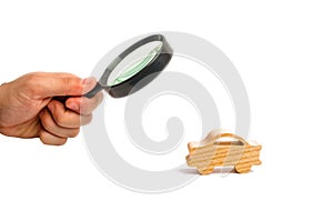 Magnifying glass is looking at the Wooden figurine of a car on a white background. Minimalism. The concept of car insurance, buyin