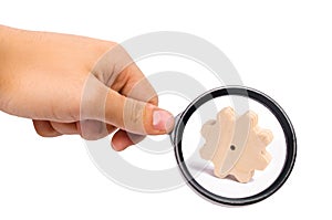 Magnifying glass is looking at the Wooden gear on a white background. Abstract background for presentations and banners.