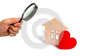 Magnifying glass is looking at the Wooden house with a red heart on a white background. Affordable housing. Family psychology.