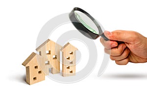 Magnifying glass is looking at the Wooden houses on a white background. The concept of rising prices for housing or rent. Growing