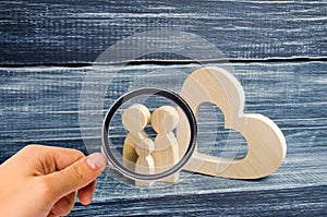 Magnifying glass is looking at the young family with a child is standing near a wooden heart. Love and loyalty,