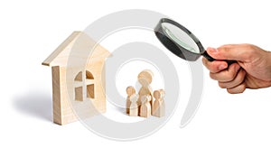 Magnifying glass is looking at the young family with children is standing near a wooden house. concept of a strong family,