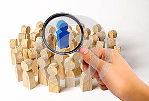 A magnifying glass looks at the blue figure of a man in the center of a crowd of people. Leadership and team management