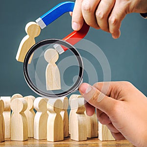 A magnifying glass looks at a magnet pulling wooden figures of people from the crowd. Recruiting new workers, headhunters.