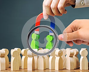 A magnifying glass looks at a magnet pulls green figures of people out of the crowd. Recruiting new workers. Formation of a new