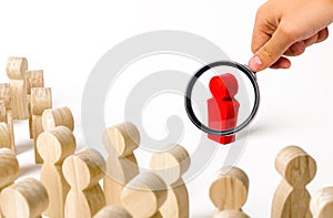 A magnifying glass looks at a red figurine of a man near a crowd. Leader, leadership and initiator of action. work or business