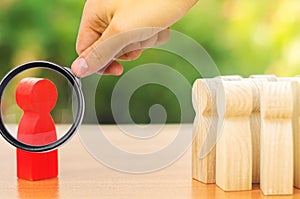 A magnifying glass looks at a red figurine of a man stands aside from the crowd of people. Asociality, sociopathy photo