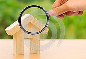 A magnifying glass looks at a wooden house. The concept of buying and selling real estate, renting. Search for a house. Affordable
