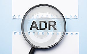 Magnifying glass loupe with sign adr between two paper sheets on the blue table