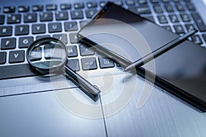 Magnifying glass, modern mobile phone with stylus on laptop computer keyboard