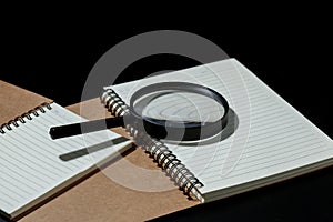 magnifying glass and notebook on black background, investigate c photo