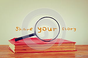 Magnifying glass , old book with the phrase share your story. filtered image.