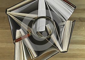 Magnifying glass over books on wood table, top view. Reading and studying concept
