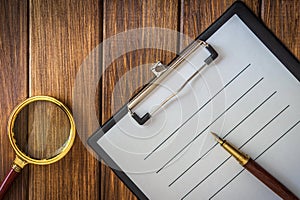 Magnifying glass and paper sheet with empty to do list and pen on an old wooden table