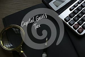 Magnifying glass, pen, calculator and notebook written with Capital Gains Tax. Business and finance concept