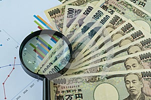 Magnifying glass on pile of japanese yen banknotes with printed